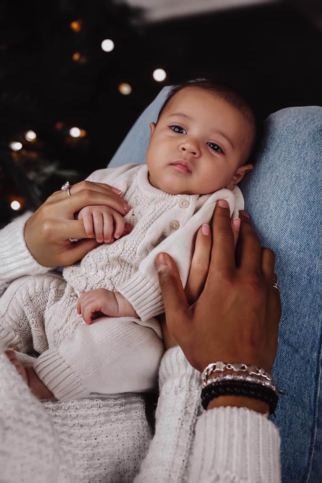 Close portrait of a newborn in a cream knit sweater held in mother’s arms