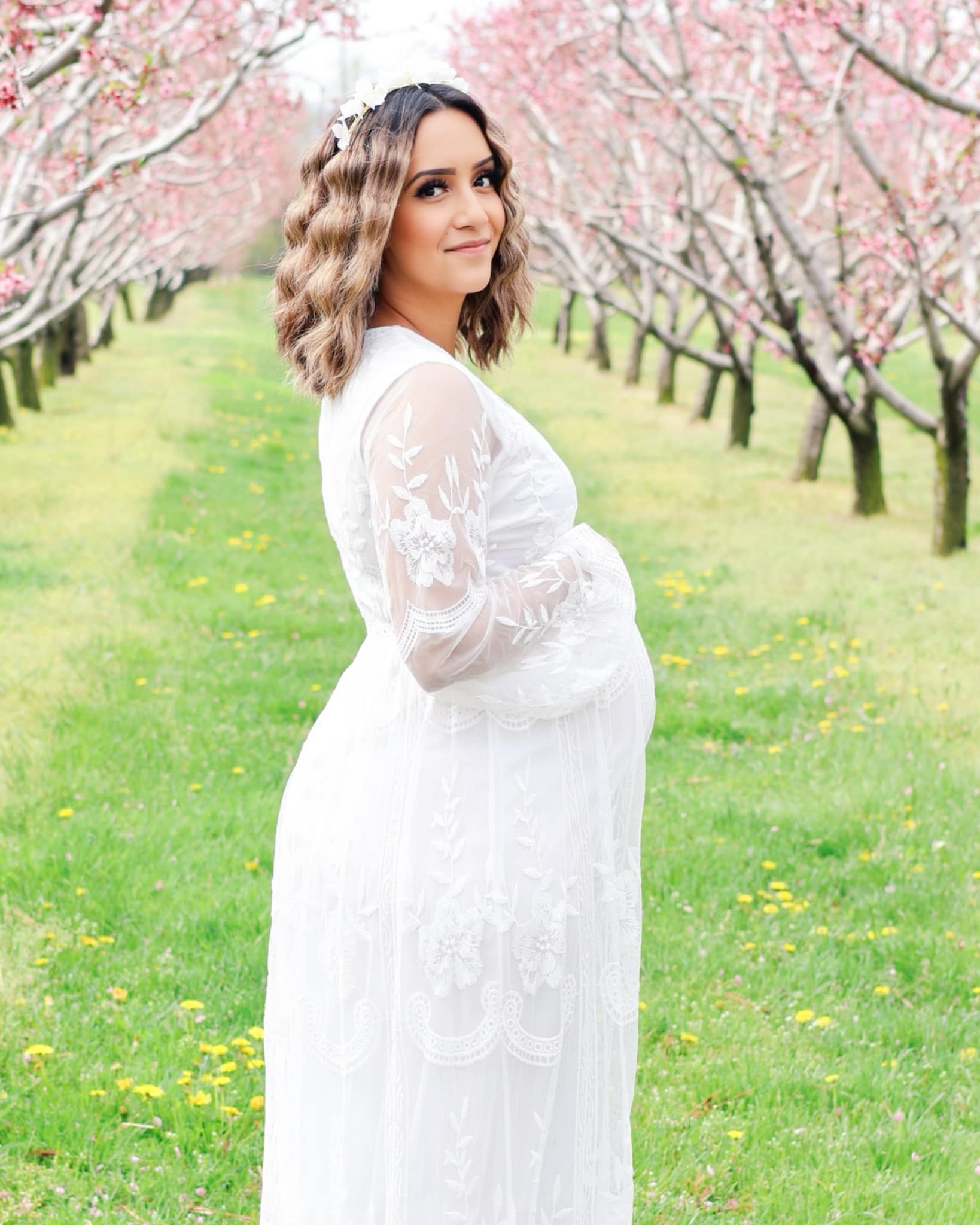 Expectant mother in white lace dress surrounded by pink cherry blossoms in a Niagara orchard