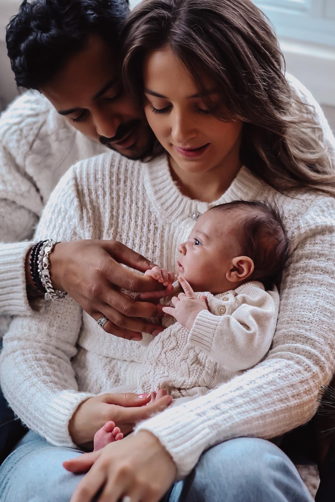 Parents holding their newborn baby in cream knit sweaters, soft in-home lifestyle portrait